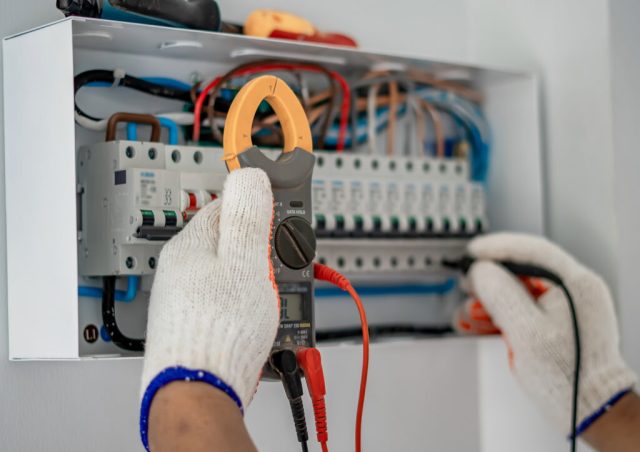 A man in gloves inspects an electrical panel while conducting a safety report for a property’s electrical installation.